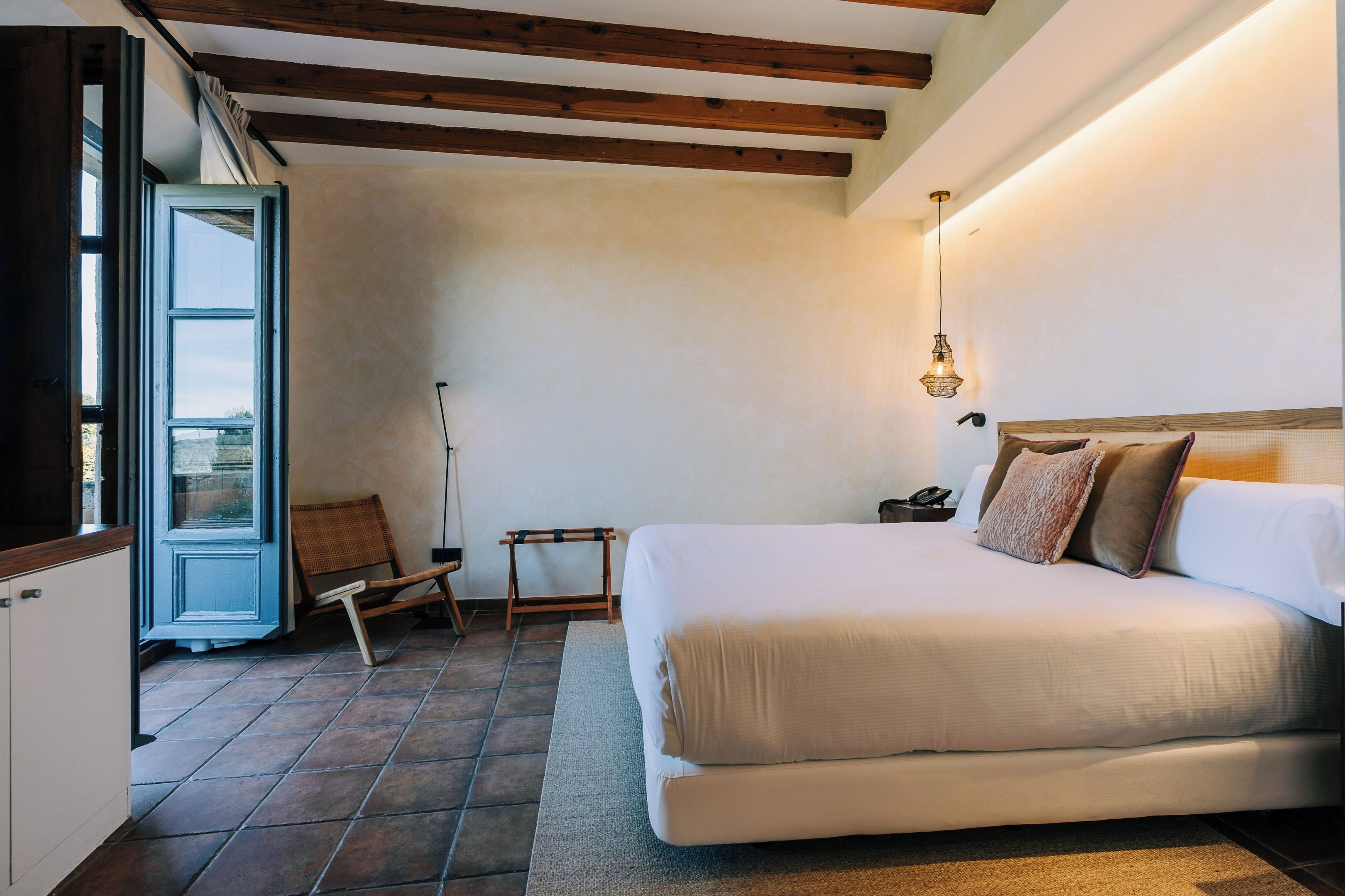 Une chambre à coucher avec un grand lit, une chaise, une petite table et une fenêtre avec des rideaux.