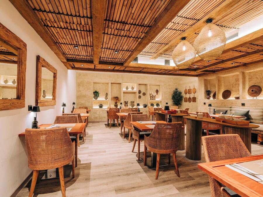 Un restaurant amb taules i caires de fusta, un sostre alt amb bigues de bambú i diverses decoracions murals.