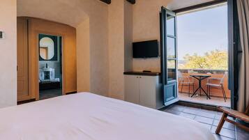 Habitación de hotel con una cama grande, televisión y puerta abierta que da a un balcón con sillas y mesa.