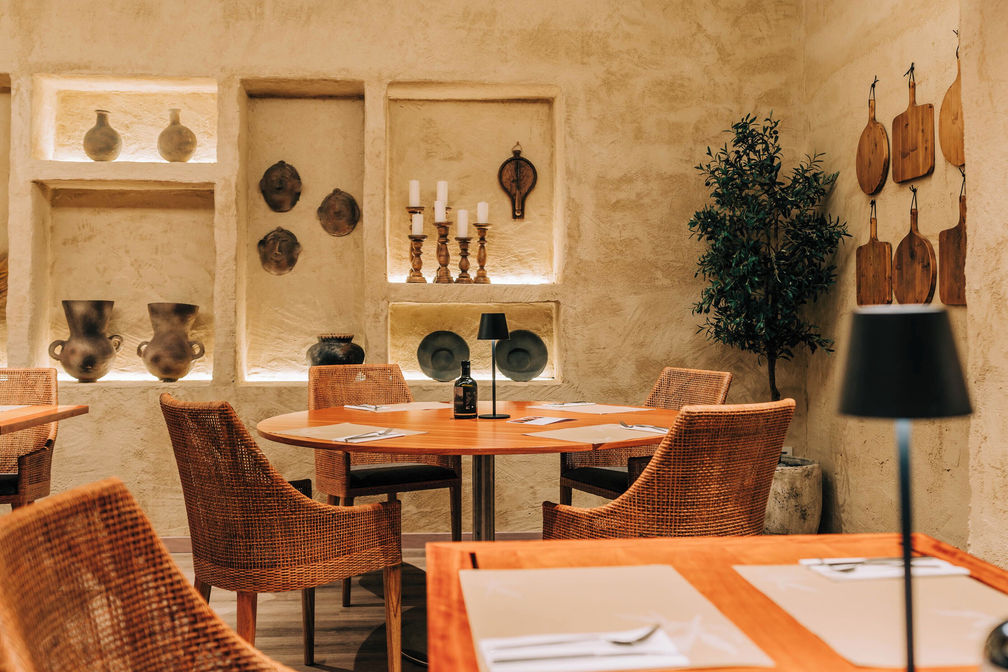 Ein Restaurant mit runden Tischen, Korbstühlen und an der Wand befestigter Keramik.