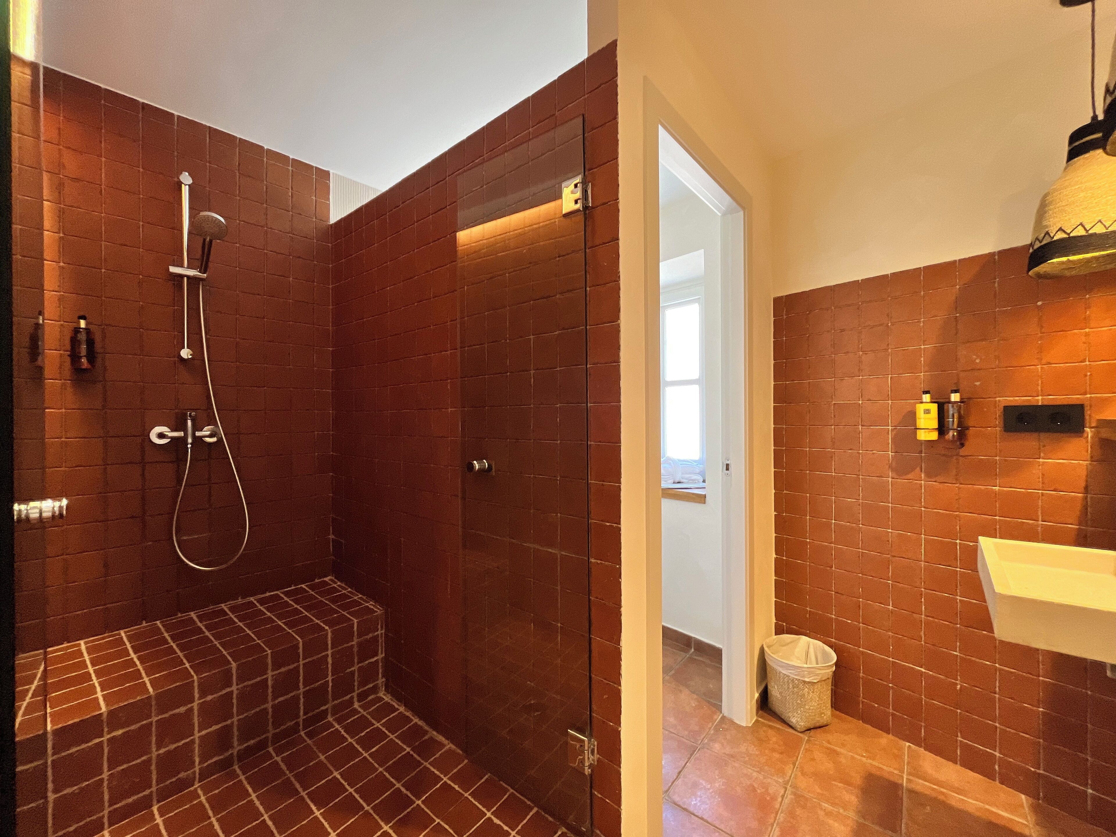 A modern bathroom with a shower, a sink, and a trash bin.