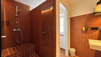 A modern bathroom with a shower, a sink, and a trash bin.