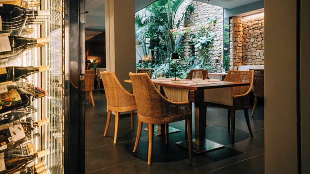A restaurant with a glass wall, wicker chairs, a stone wall, and a view of greenery. - Gran Claustre Boutique Hotel & SPA (Altafulla)