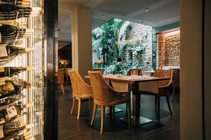 Un restaurant doté d’un mur en verre, de chaises en osier, d’un mur en pierre et offrant une vue sur la verdure.
