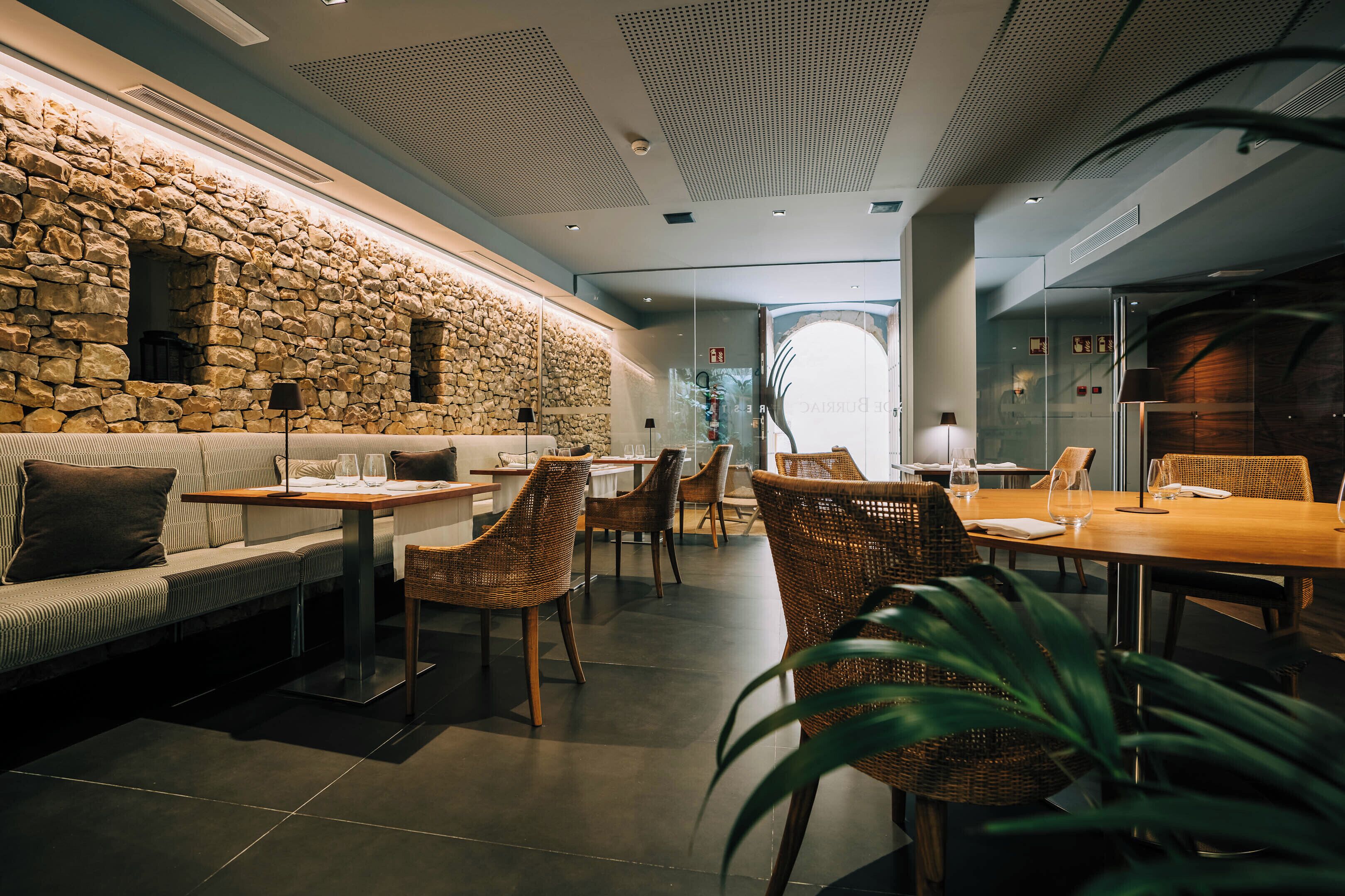 Un restaurant moderne avec des murs en pierre, des meubles en osier et différents types de sièges, notamment des tables et un canapé.