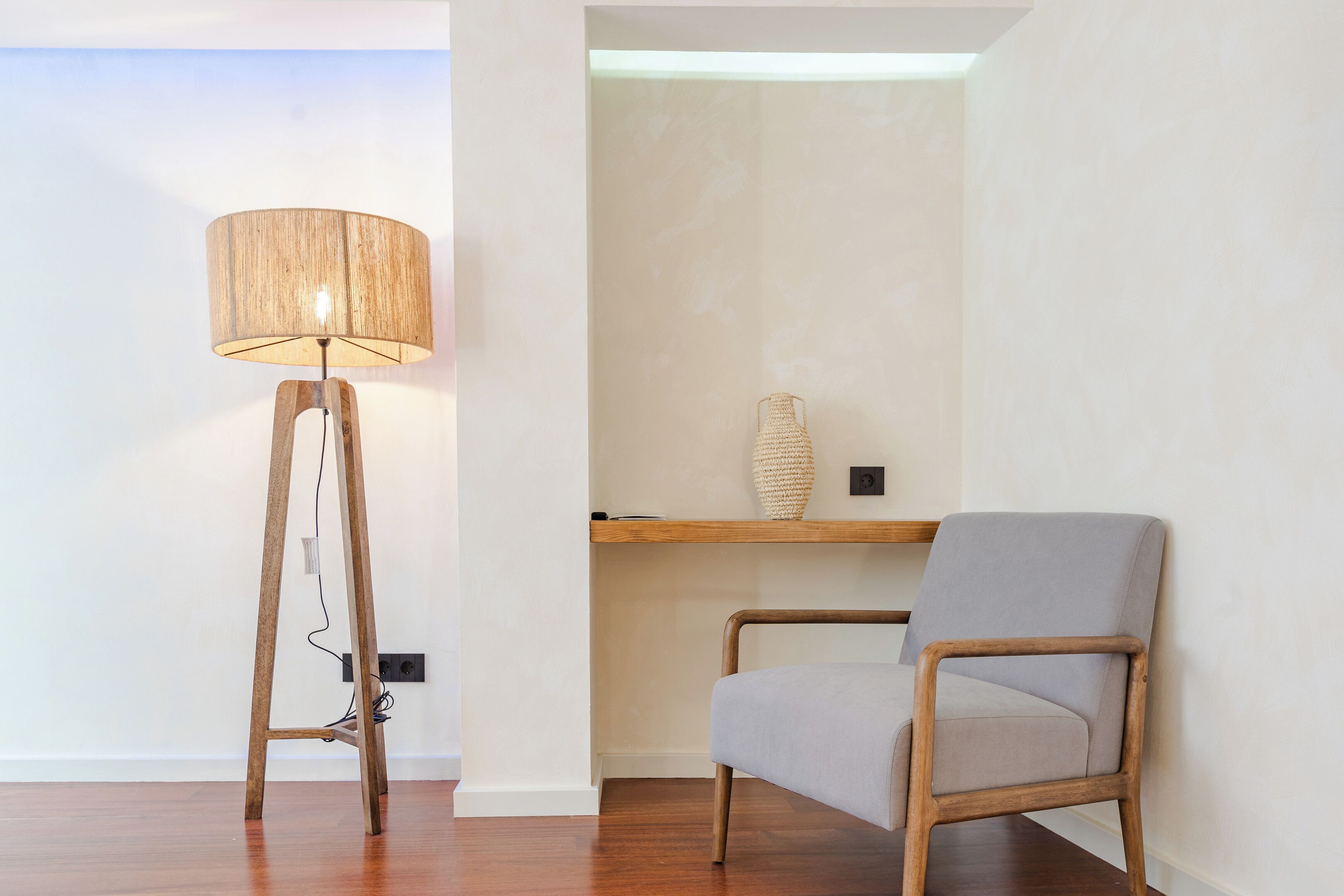 Een kamer met een vloerlamp, een stoel en een plank met een vaas.