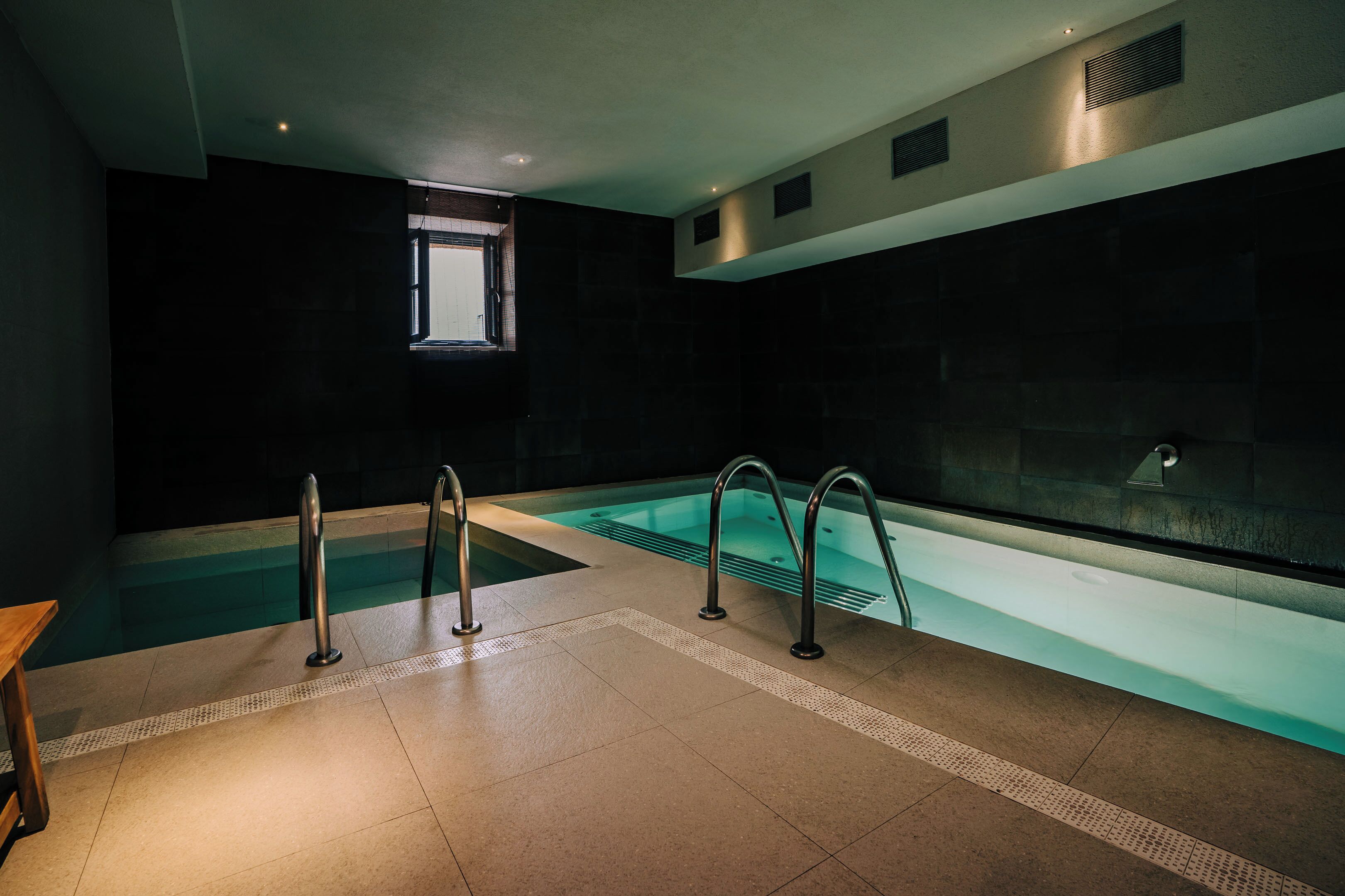 Una piscina interior moderna con agua cristalina, barandales de metal y suelo de baldosas.