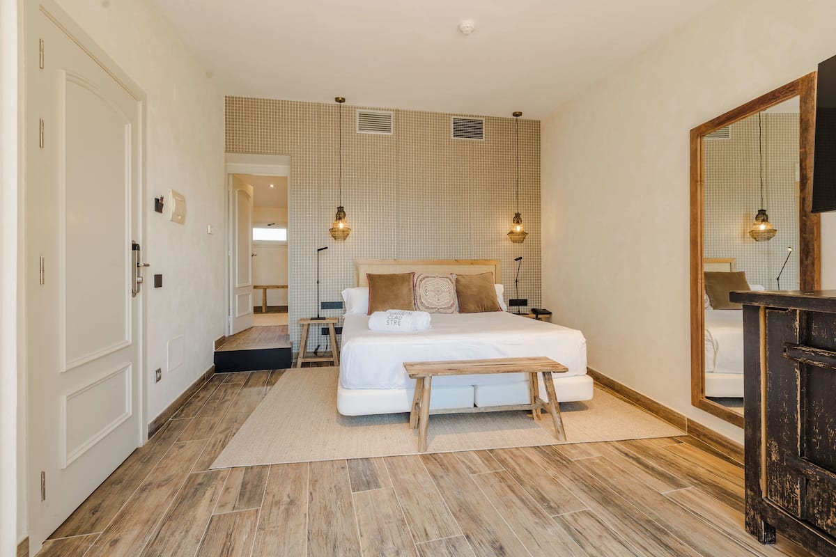 Une chambre à coucher avec un grand lit, des tables de chevet, un banc en bois, un miroir et une armoire.