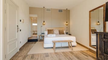 Un dormitorio con una cama grande, mesitas de noche, un banco de madera, un espejo y un armario.
