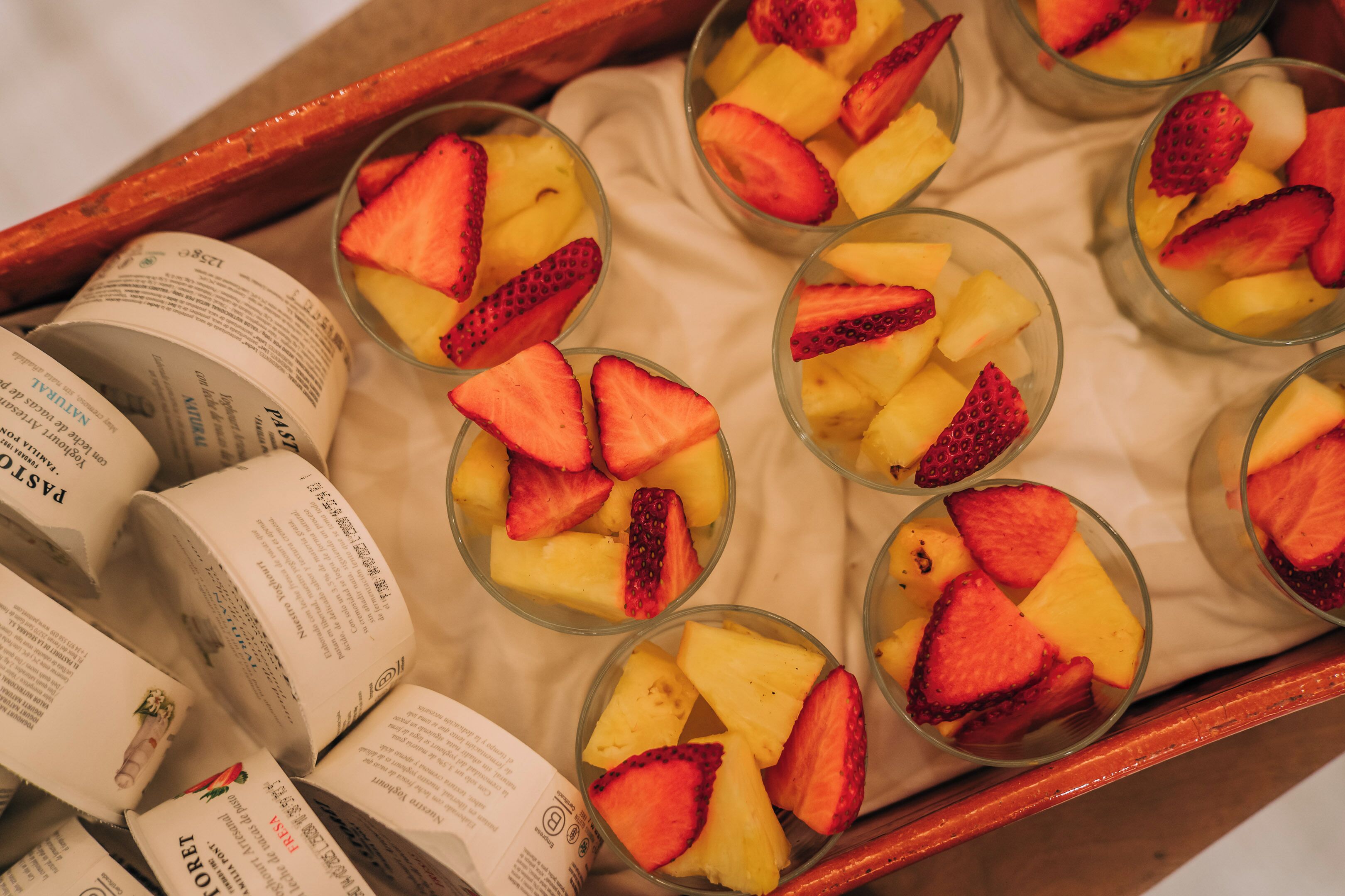 A tray of fruit cups with strawberries and pineapple slices, accompanied by rolled-up menus.