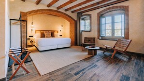 A bedroom with a large bed, a wooden chair, a small table, and a window. - Gran Claustre Boutique Hotel & SPA (Altafulla)