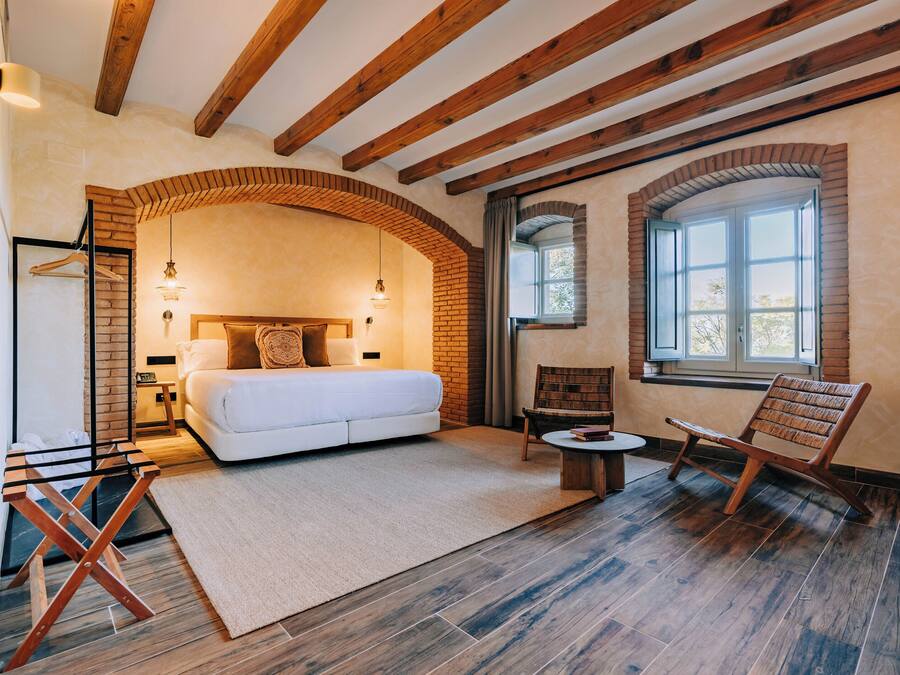 Ein Schlafzimmer mit einem großen Bett, einem Holzstuhl, einem kleinen Tisch und einem Fenster.