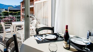 A dining table set for two with a bottle of wine, glasses, and plates on a balcony overlooking a mountain. - Residence Foch (Lourdes)