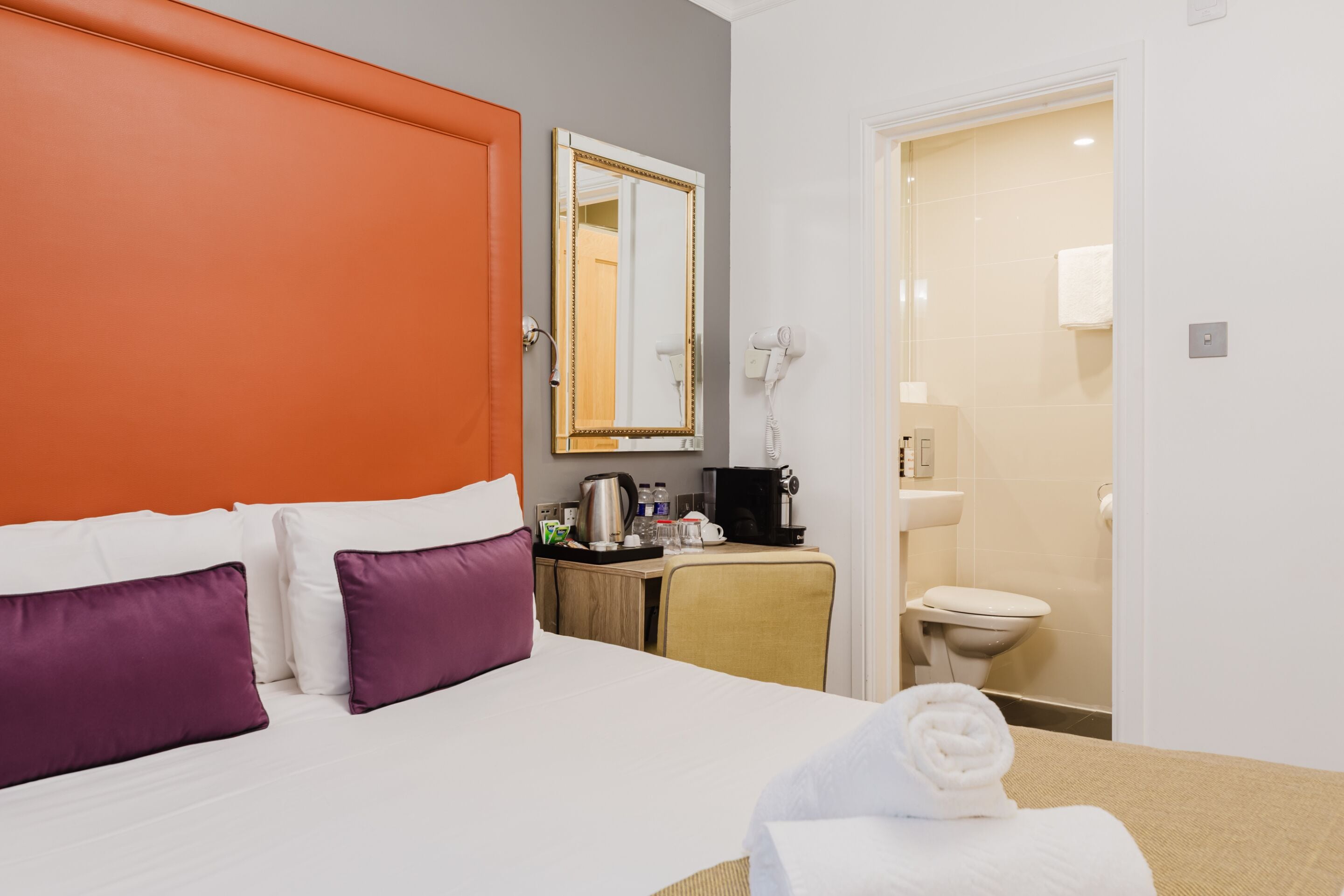 Une chambre d’hôtel avec un lit, un bureau doté d’une machine à café, un miroir et une salle de bain visible à travers une porte ouverte.