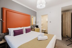 A hotel room with a large bed, a wooden wardrobe, a bathroom with a toilet and sink, and a small desk with a kettle. - The Porchester Hotel (London)