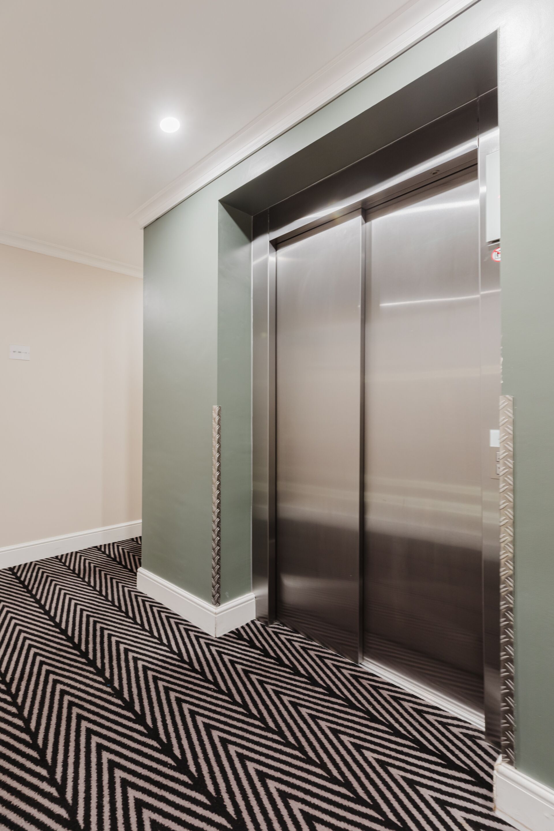 An elevator in a hallway with patterned flooring and light-colored walls.