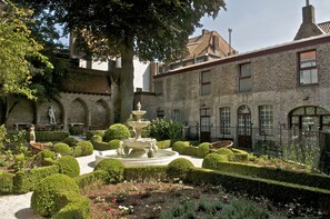 Ein Innenhof mit Brunnen, ordentlich geschnittenen Hecken und einem Backsteinhaus mit Rundbogenfenstern.