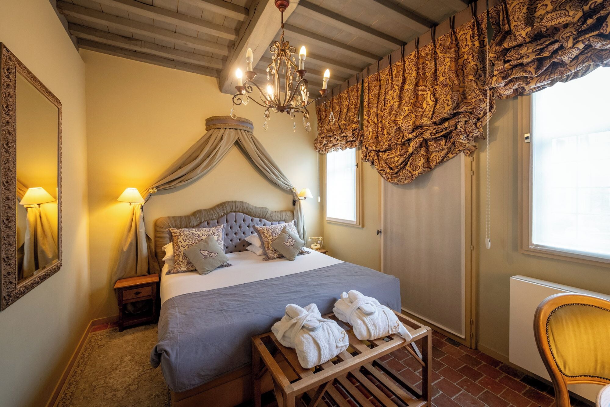 A bedroom with a large bed, a chandelier, a mirror, and a window with curtains.