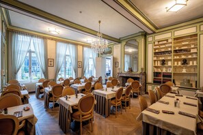 A dining area with multiple tables and chairs, a chandelier, and a fireplace. - Hotel Jan Brito (Bruges)