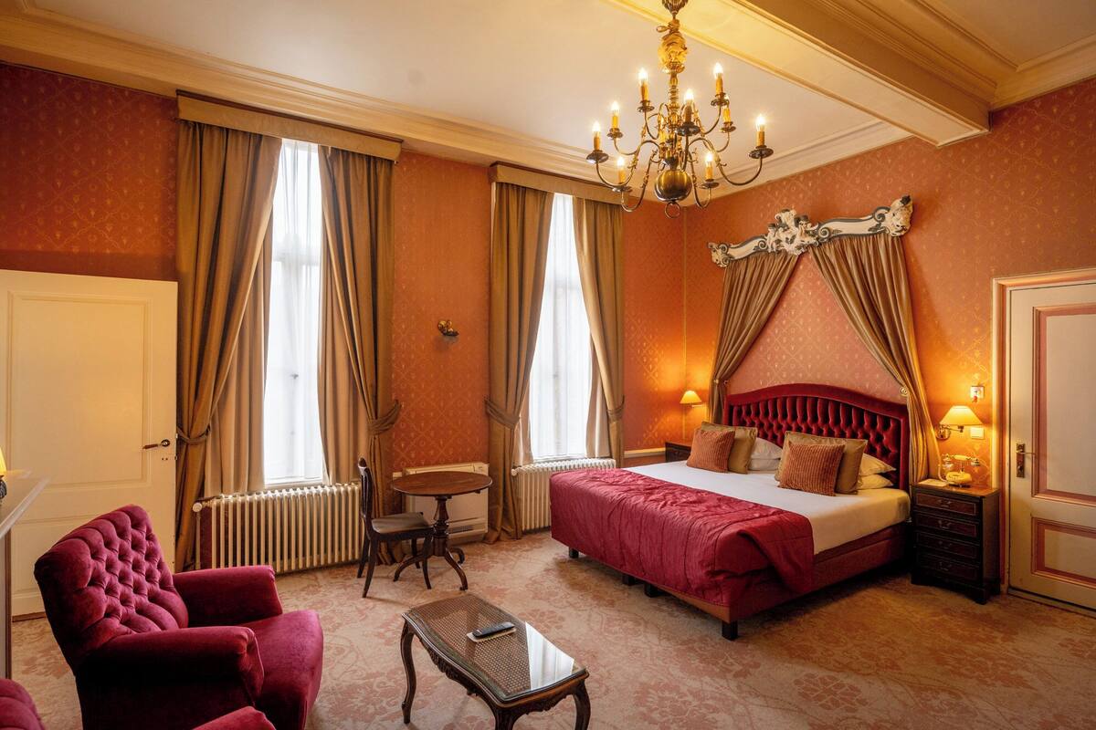 Un dormitorio amplio con una cama grande, una zona de estar con una silla y una mesa, y un candelabro.