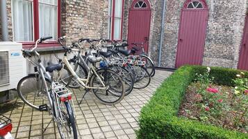 A courtyard with multiple bicycles parked against a brick building with red doors and windows.