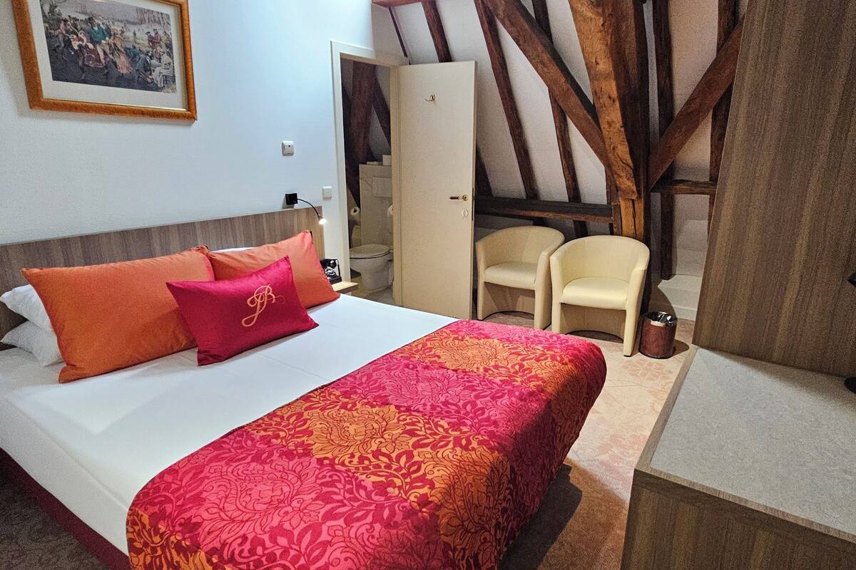 Un dormitorio con cama, una silla, armario y espejo.