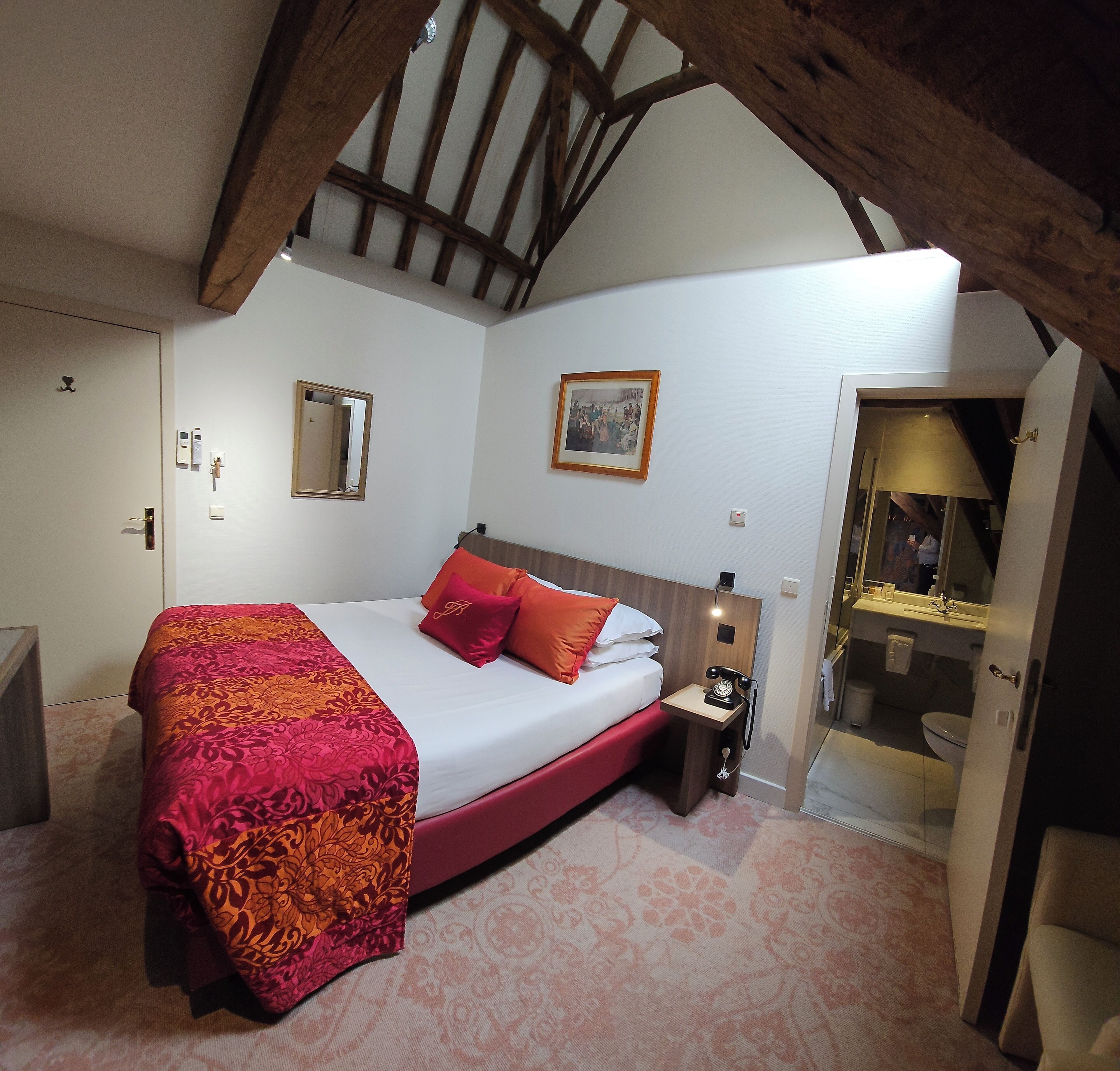 Ein Schlafzimmer mit einem großen Bett, einem Nachttisch, einem Spiegel und einem durch eine offene Tür einsehbarer Badezimmer.