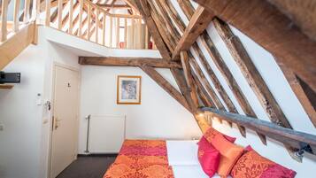 A bedroom with a sloped ceiling, wooden beams, a bed with patterned bedding, and a framed picture on the wall.