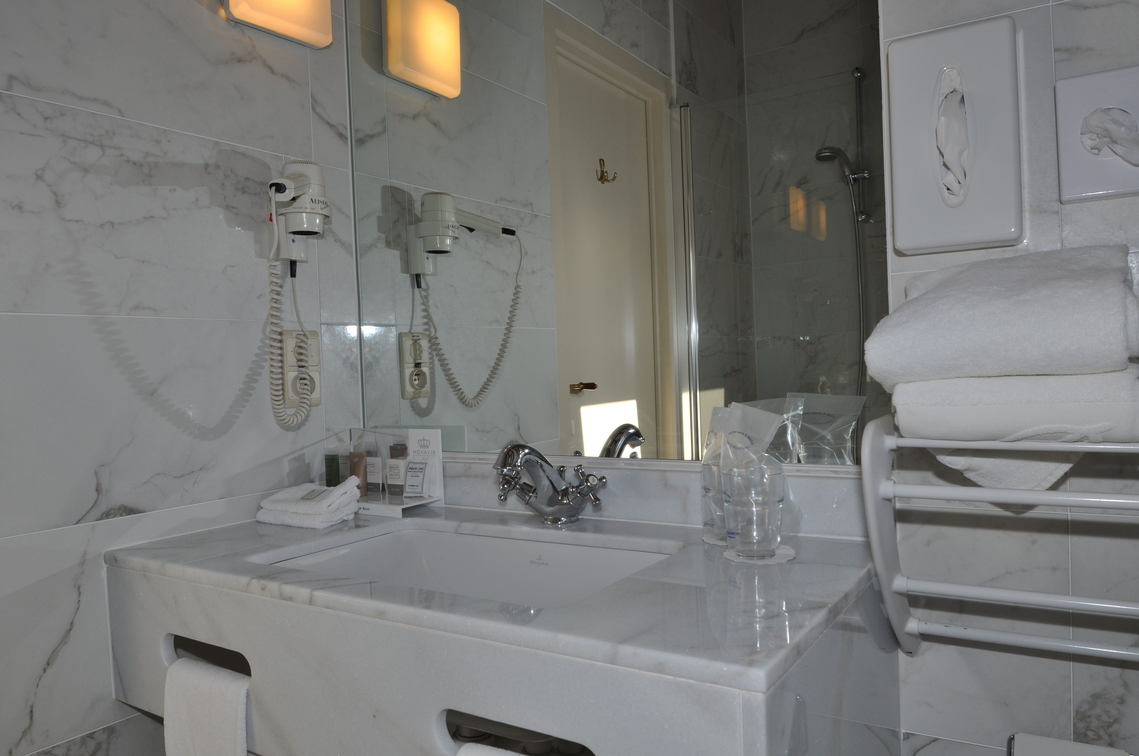 A bathroom with a marble sink, a hairdryer, a mirror, and a towel rack.