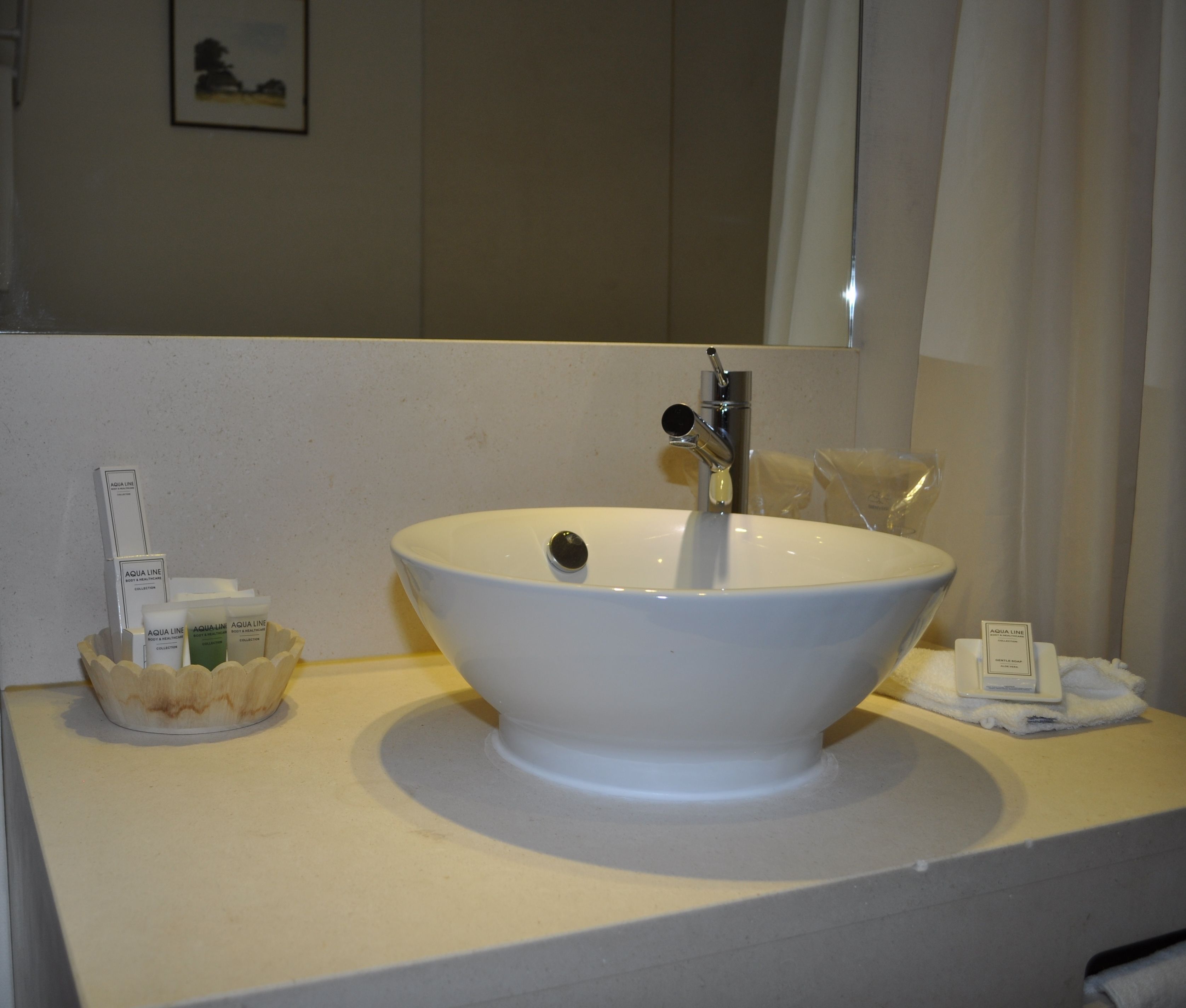 Ein Badezimmerwaschbecken mit großer Schüssel, ein Spiegel darüber und Pflegeprodukten auf der Ablagefläche.