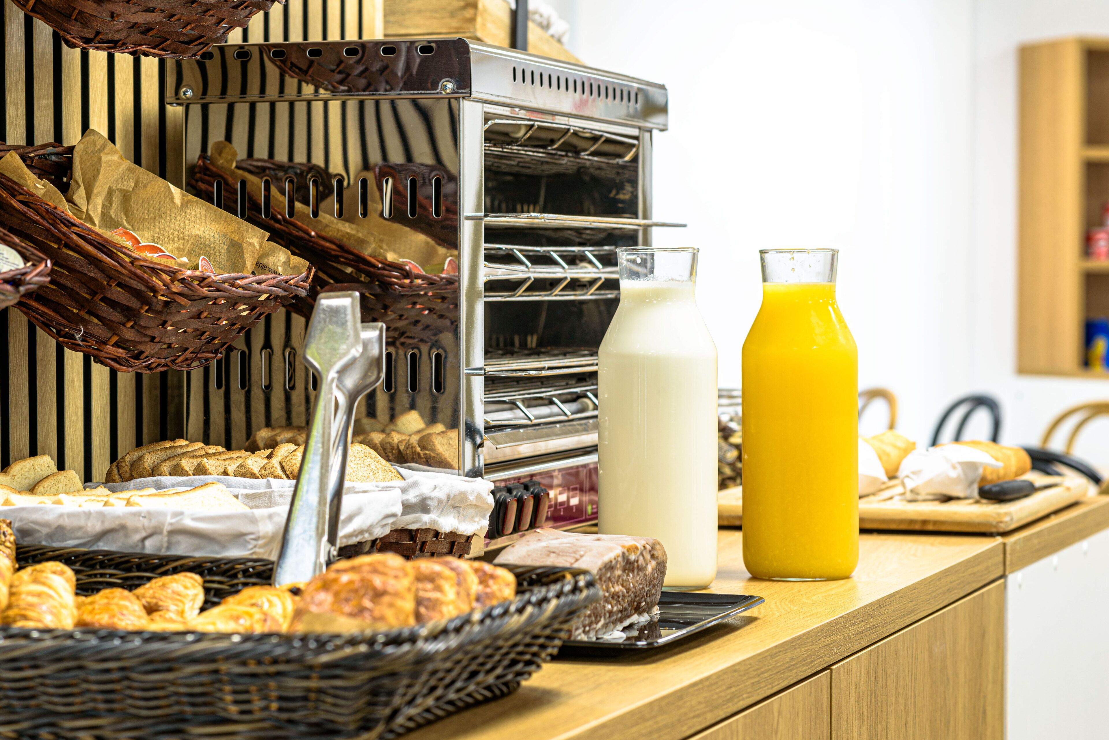 A breakfast buffet with various breads, pastries, and a glass of orange juice.