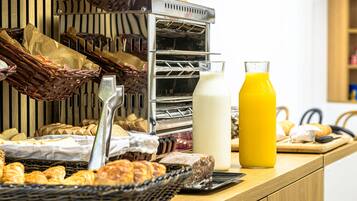 A breakfast buffet with various breads, pastries, and a glass of orange juice.