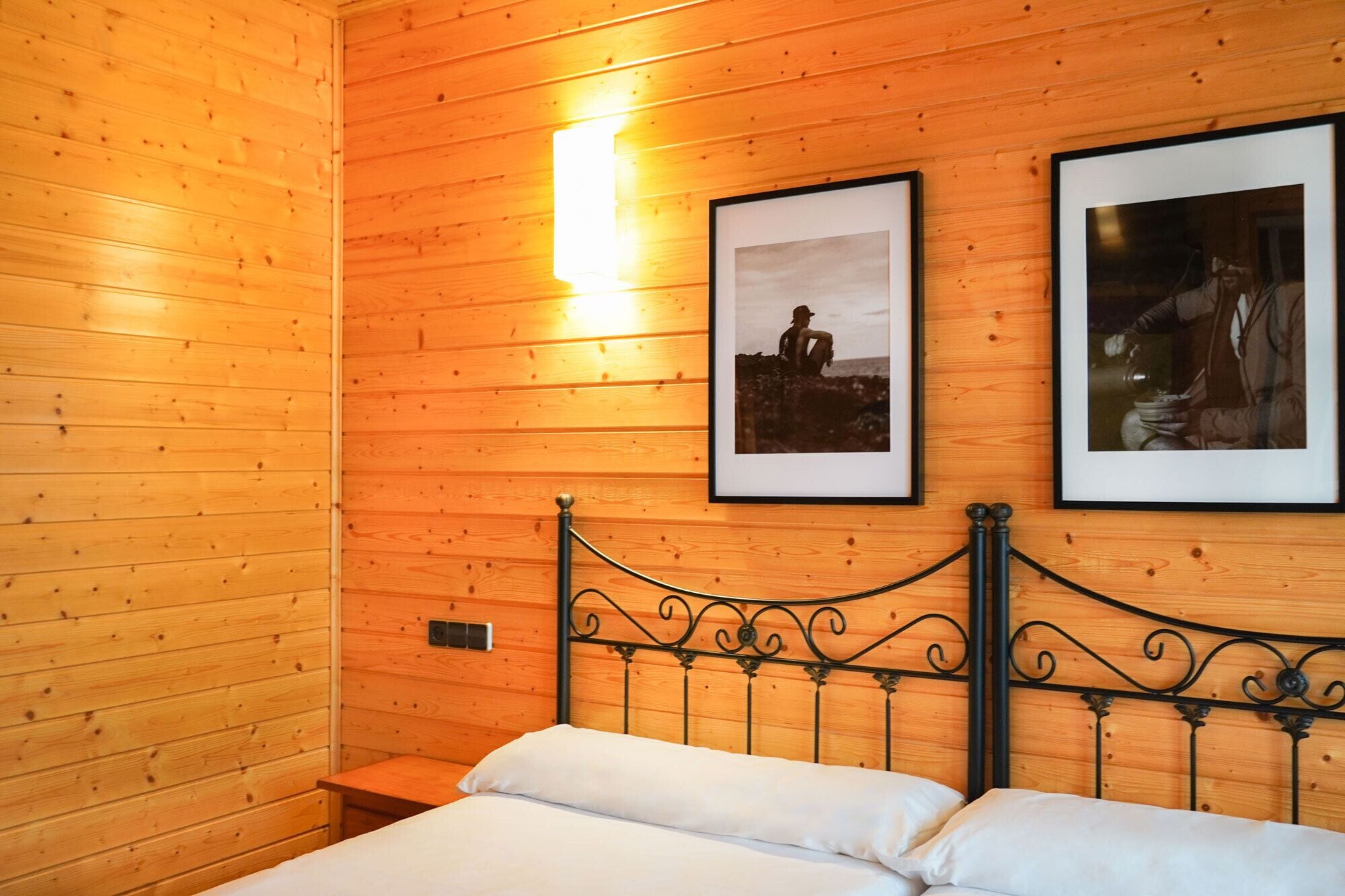A wooden cabin room with a bed, two framed pictures on the wall, and a nightstand.