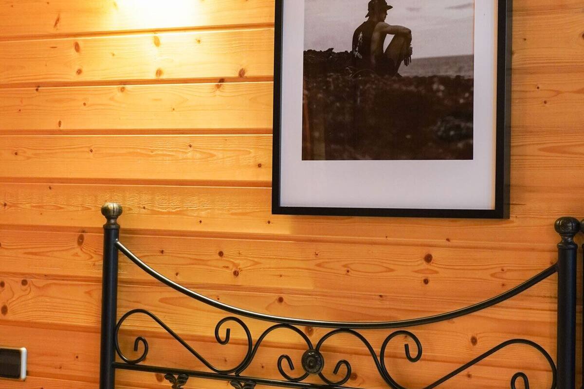 Une pièce aux murs lambrissés, avec un lit, une photographie encadrée accrochée au mur et un luminaire fixé au mur.