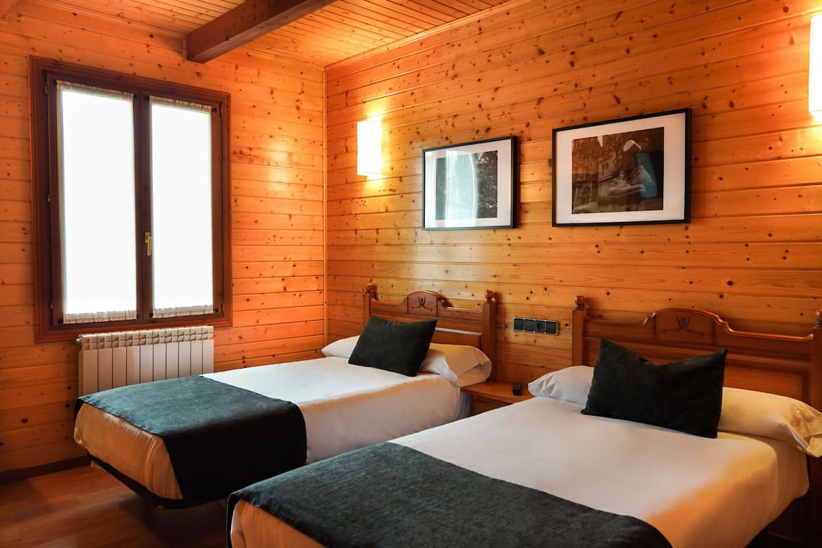 Une chambre avec deux lits, des murs en bois, un radiateur et des tableaux encadrés accrochés au mur.