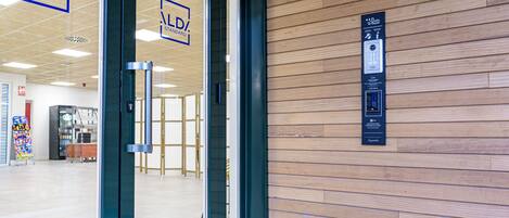 Entrada de hotel con puertas de vidrio, un muro de madera y un teclado digital para acceso a las habitaciones.