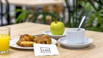 Ein Frühstückstisch mit Croissants, einem Apfel, einem Glas Orangensaft und einer Tasse mit Löffel.