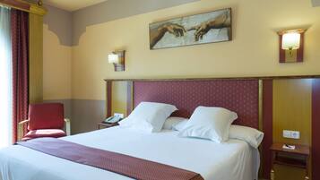 Habitación de hotel con una cama grande, un sillón rojo, una mesita de noche y un cuadro en la pared.