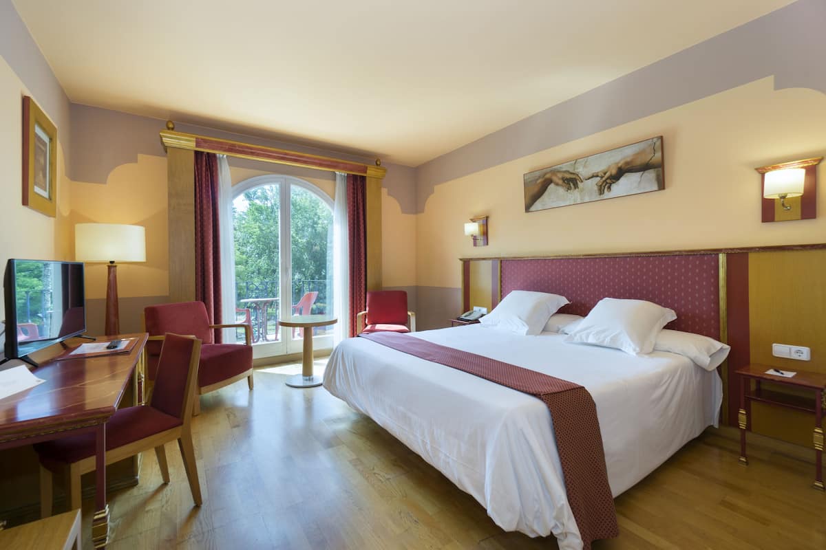 A hotel room with a large bed, a desk with a chair, a television, and a window with curtains.