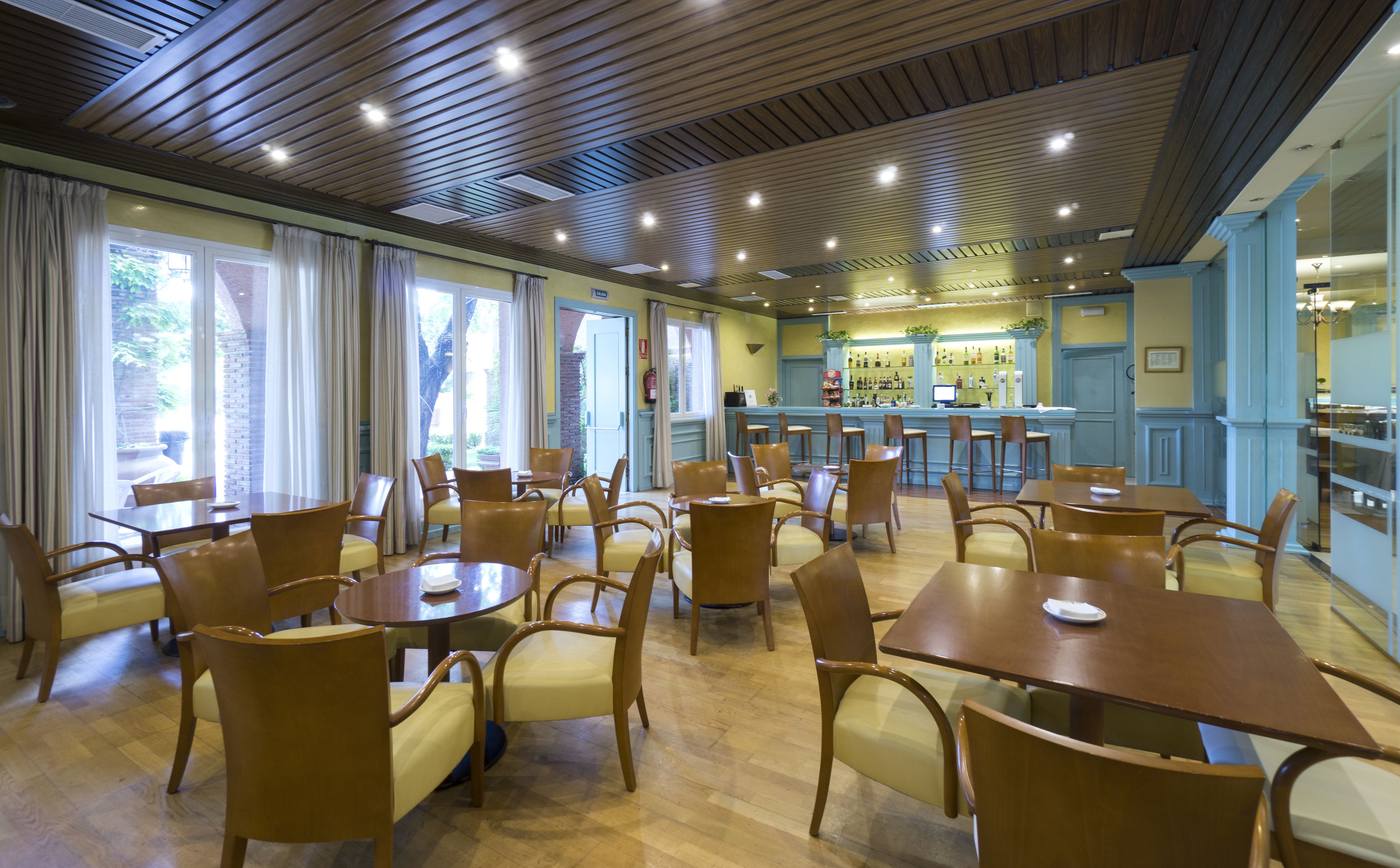 A restaurant with wooden tables and chairs, a bar area, and large windows with curtains.