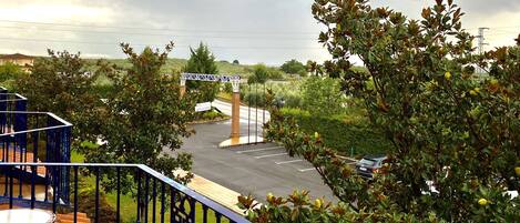 A parking area with a blue staircase leading to a building, surrounded by greenery and a cloudy sky.