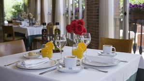 A dining table set with plates, glasses, and a coffee cup, with a vase of red flowers in the background.