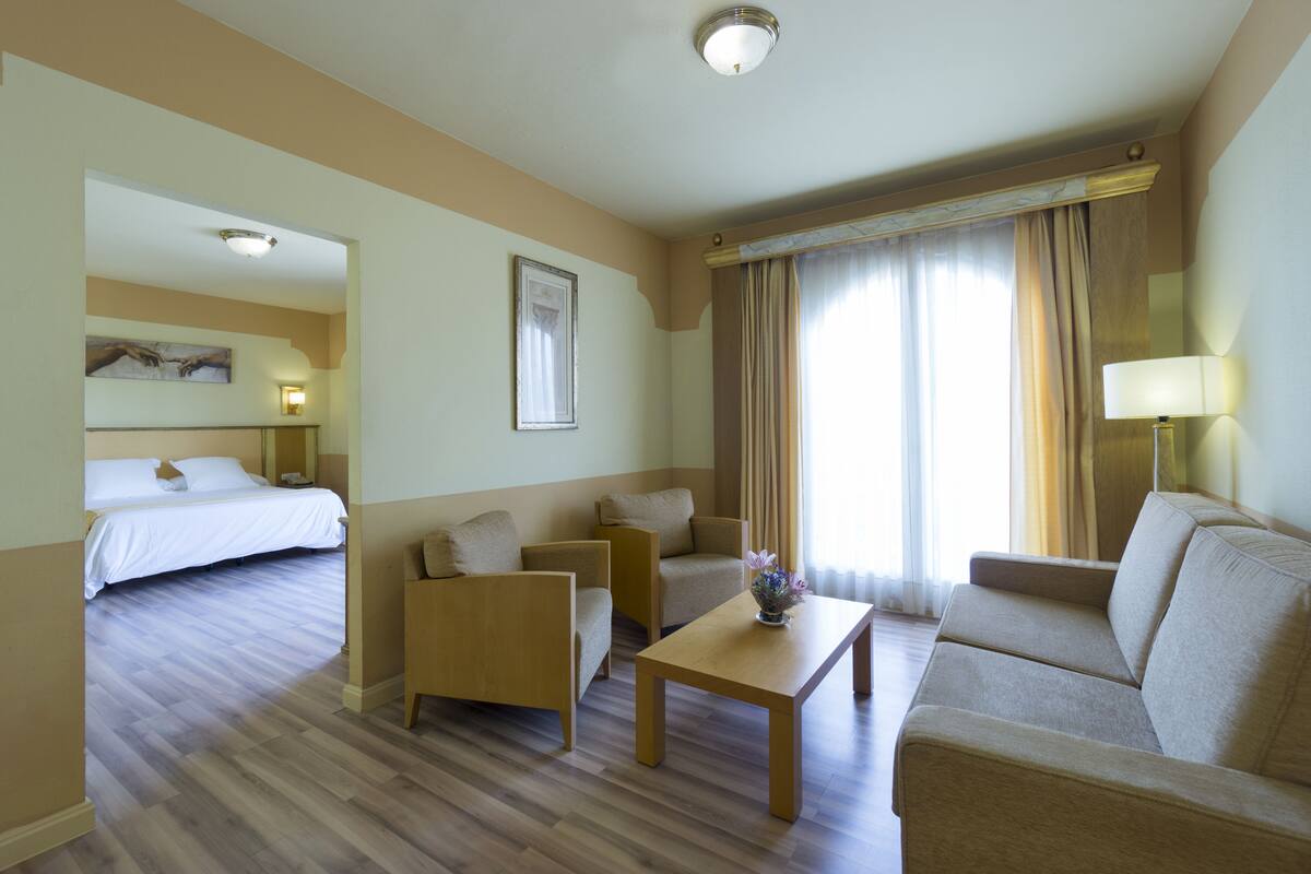 A hotel room with a bed, two sofas, a coffee table, and a lamp.