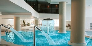 Una piscina interior con múltiples elementos acuáticos, incluyendo una cascada central y dos fuentes laterales.