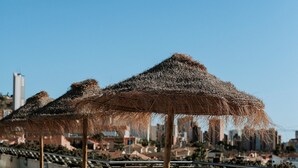 Un área de lounge en la azotea con tumbonas y sombrillas de paja, con vistas a un paisaje urbano.