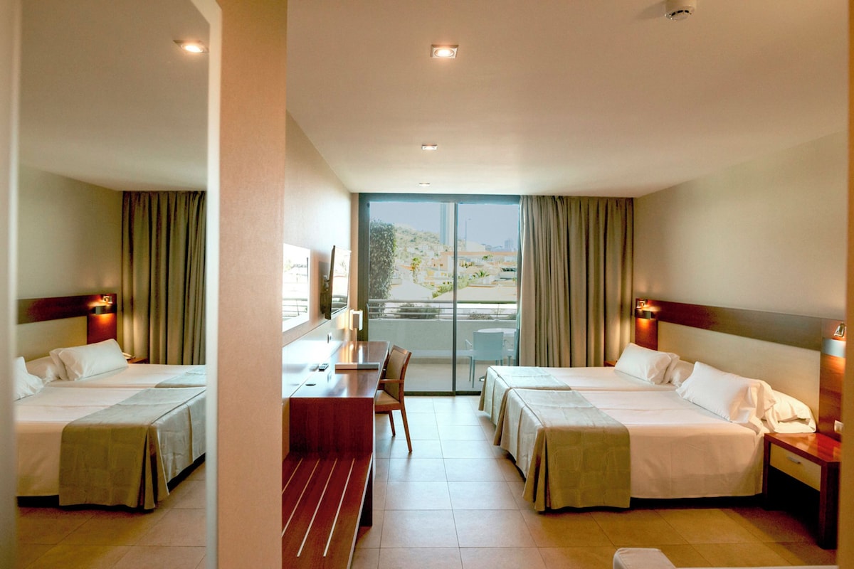 A hotel room with two beds, a desk, and a view of the outdoors.