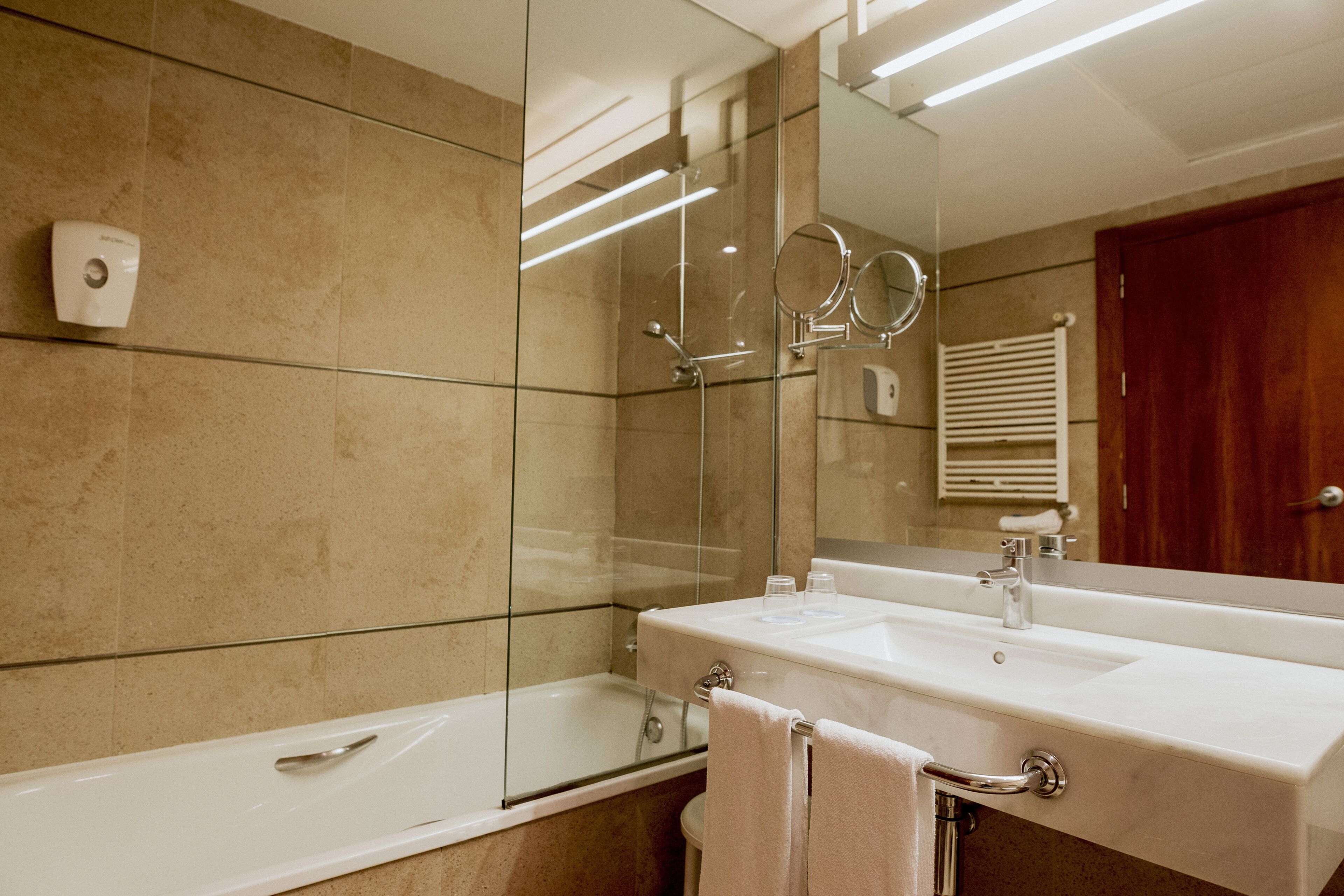 Un baño moderno con ducha de vidrio, lavabo blanco y un espejo grande.