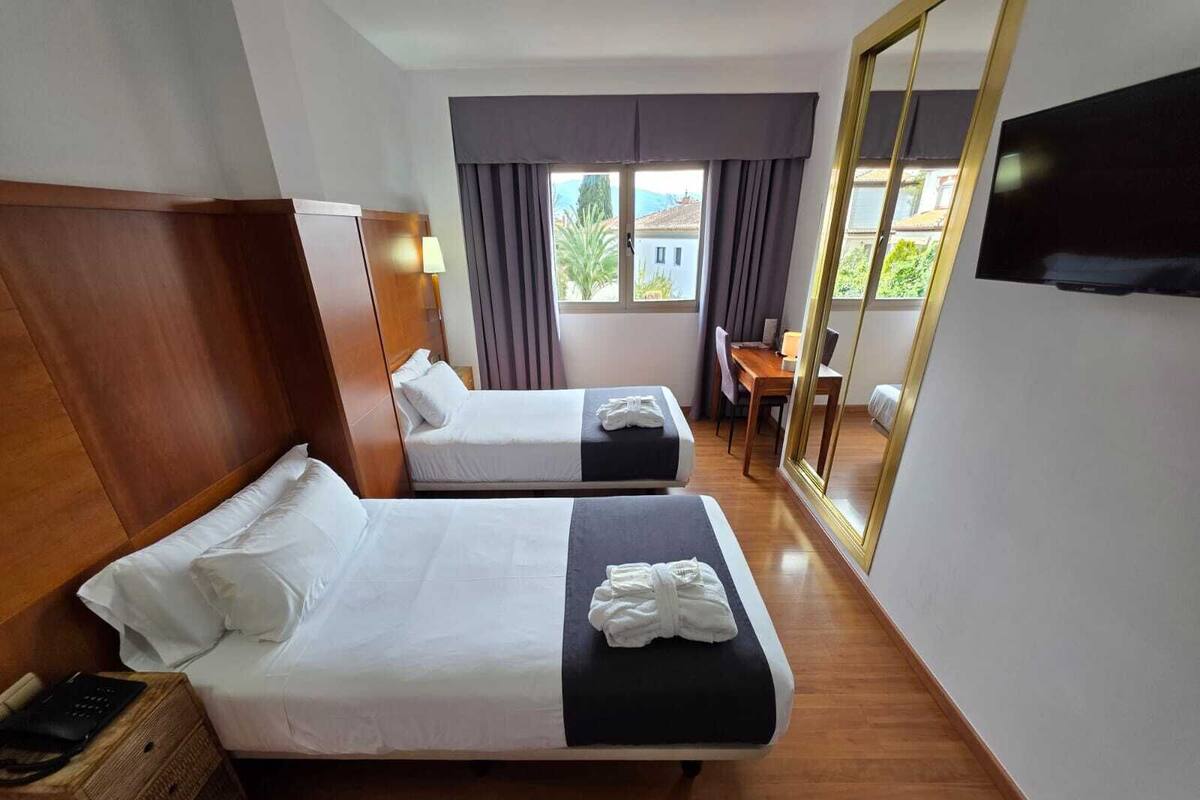 A hotel room with two beds, a desk, a chair, a TV, and a large mirror.
