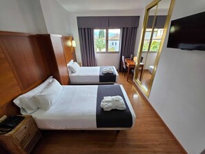 A hotel room with two beds, a desk, a chair, a TV, and a large mirror.