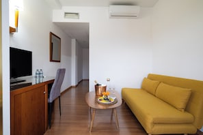 A hotel room with a wooden desk, a flat-screen TV, a sofa, a small table with fruit and drinks, and a mirror on the wall. - Hotel Saylu (Granada)